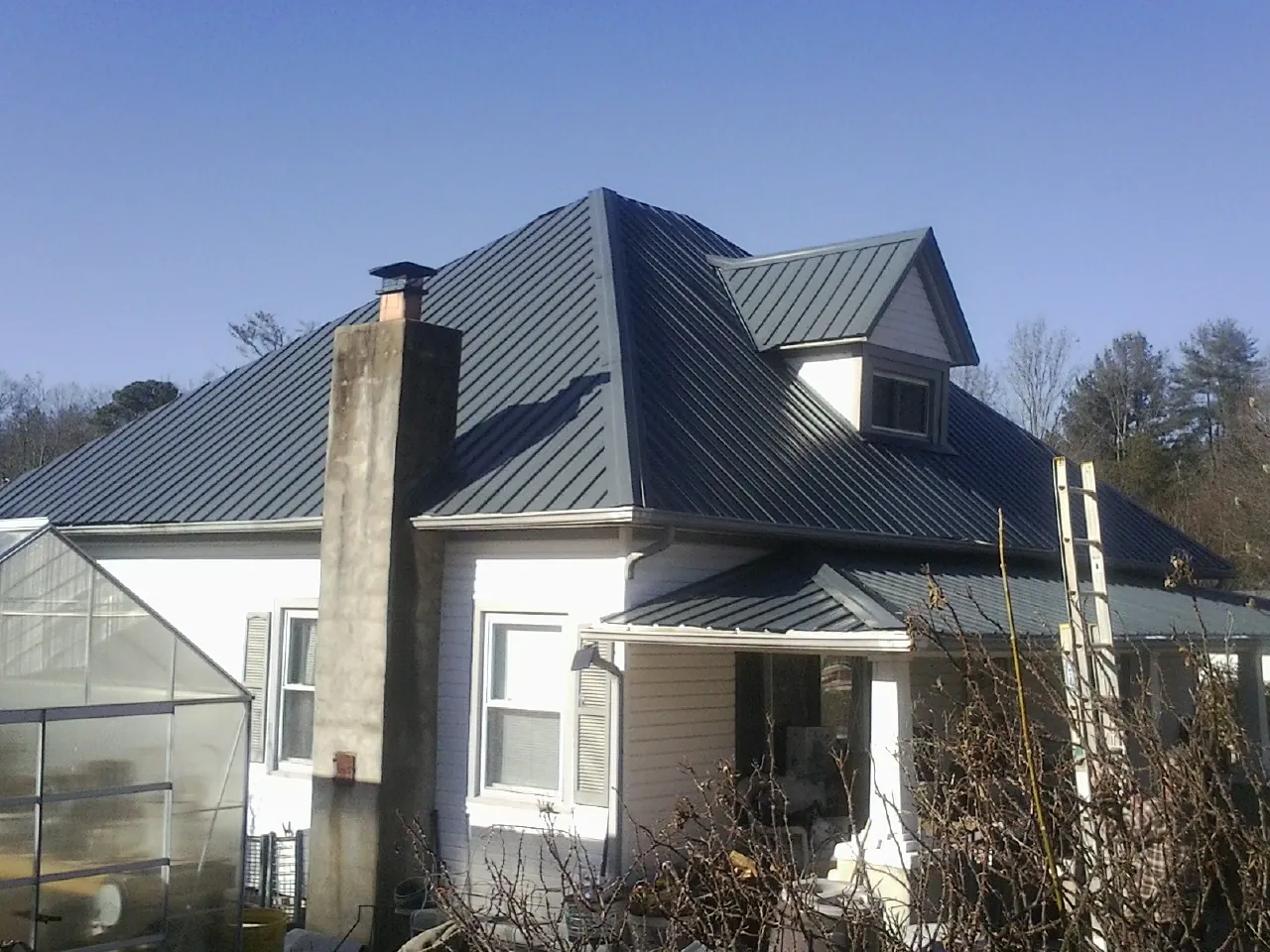 Dark blue standing seam metal roof on a white farmhouse with dormer — Slate & Tile Roof Repair by Roofing Brothers in Carroll