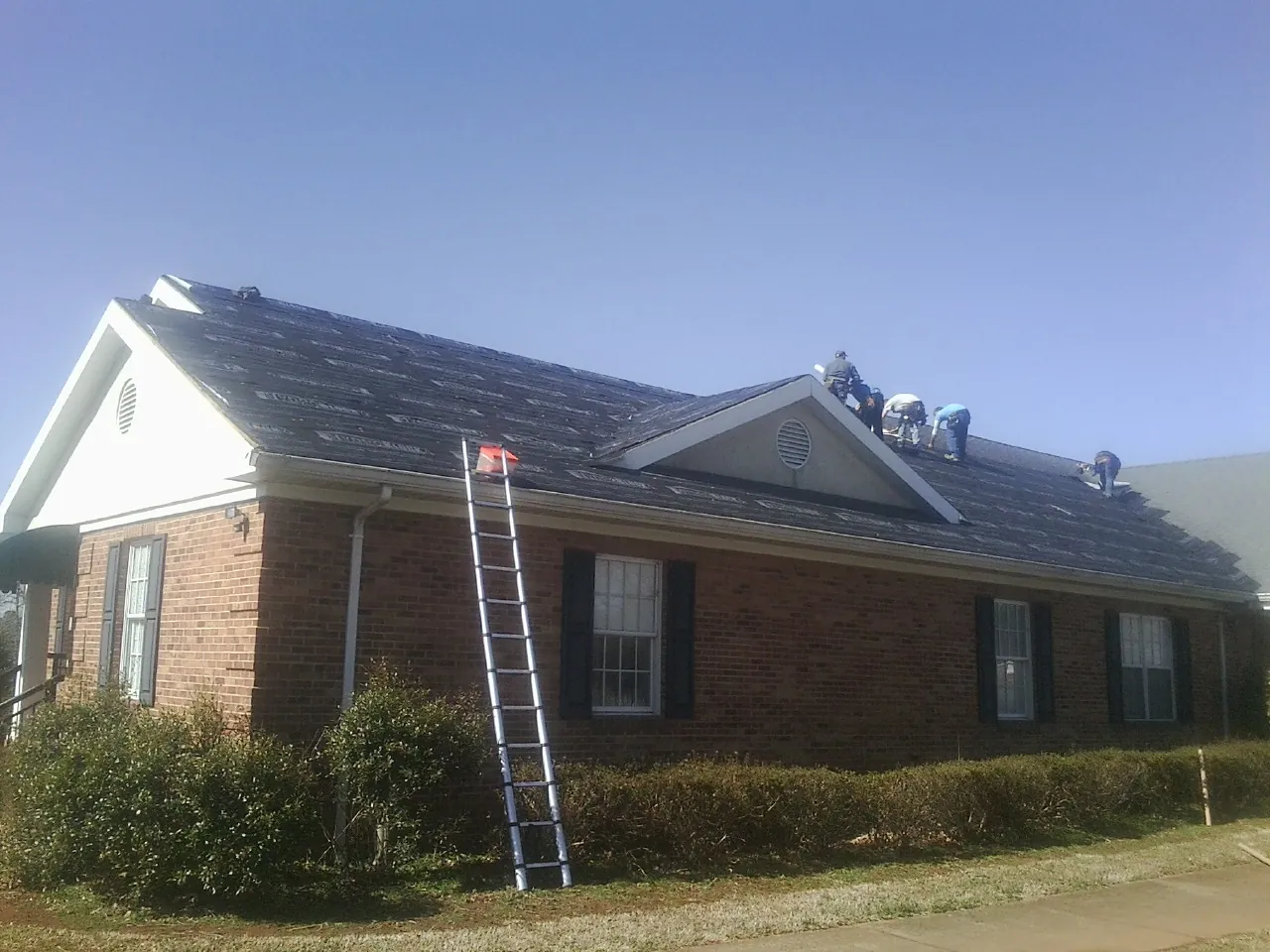 Crew tearing shingles off a brick ranch roof with a ladder set — Metal Roof Repair work by our crew in Carroll