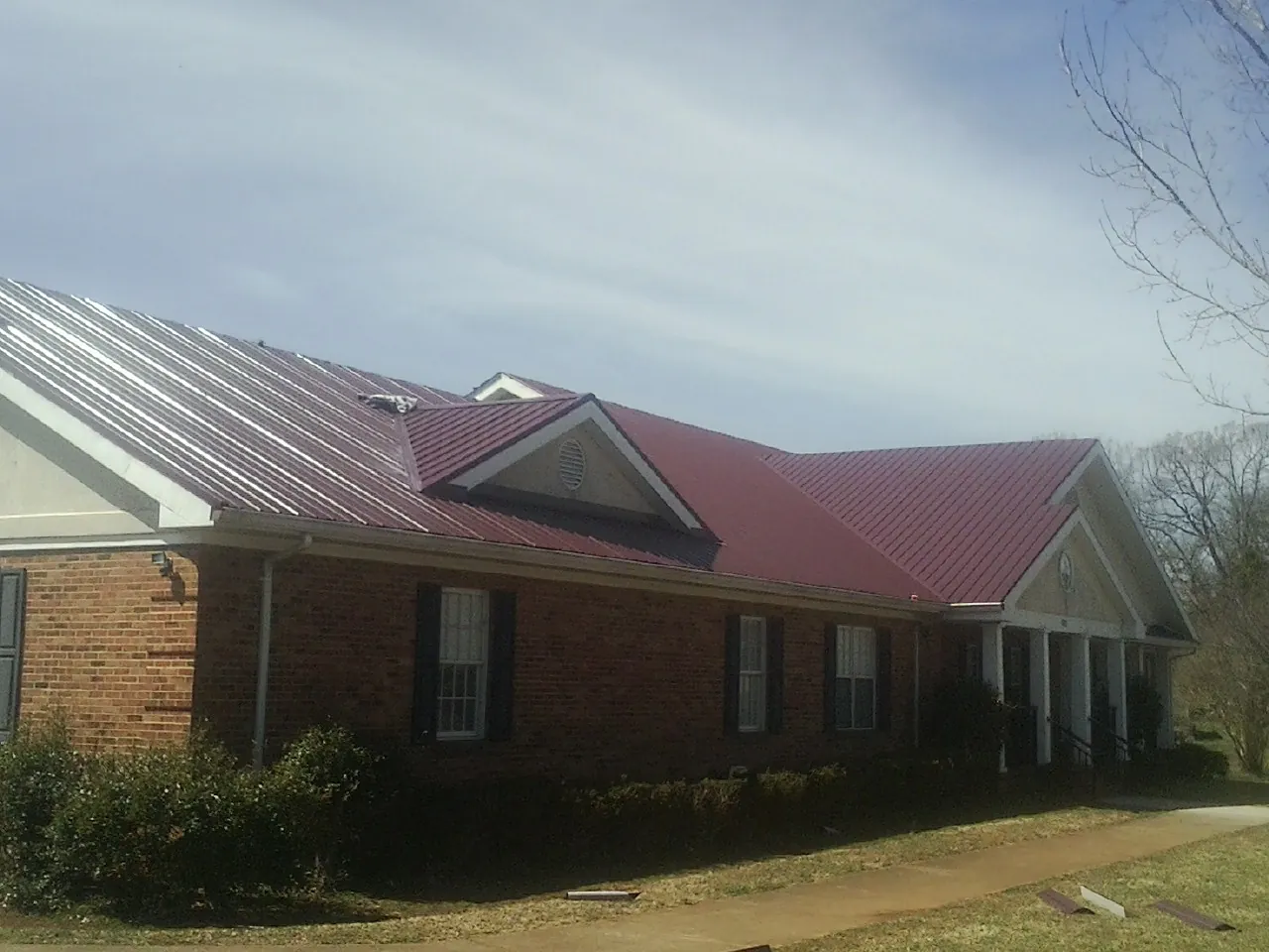 Red metal roof with gabled entries on a long brick building, from a Hail Damage Roof Repair job in Carroll