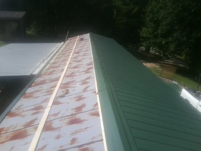 Old rusted panels beside newly installed green metal roofing — Wind Damage Roof Repair by Roofing Brothers in Carroll