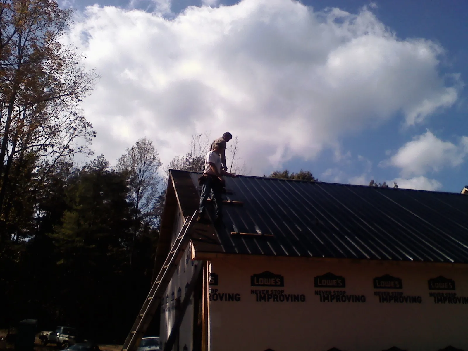 Roofer fastening dark metal panels high against a cloudy sky, from a Roof Inspection job in Carroll