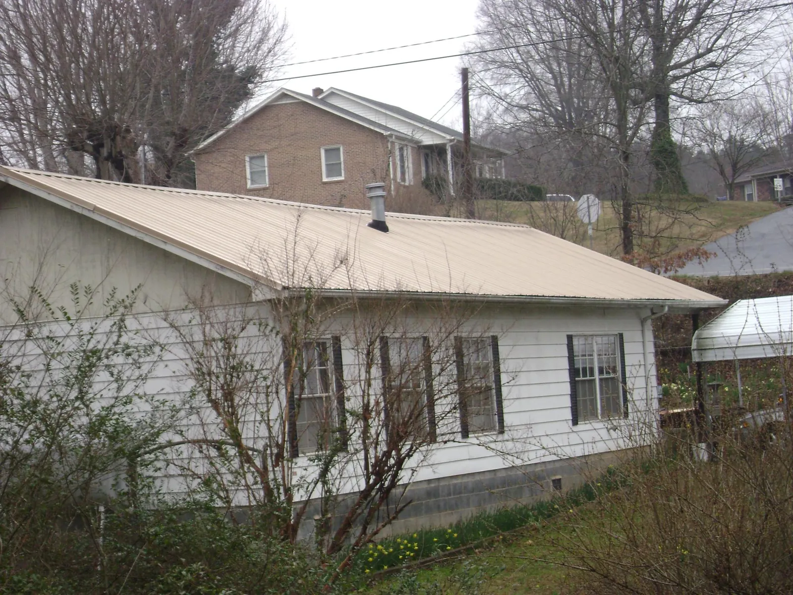Tan metal roof on a white sided house set into a hillside — Commercial Roofing by Roofing Brothers in Carroll