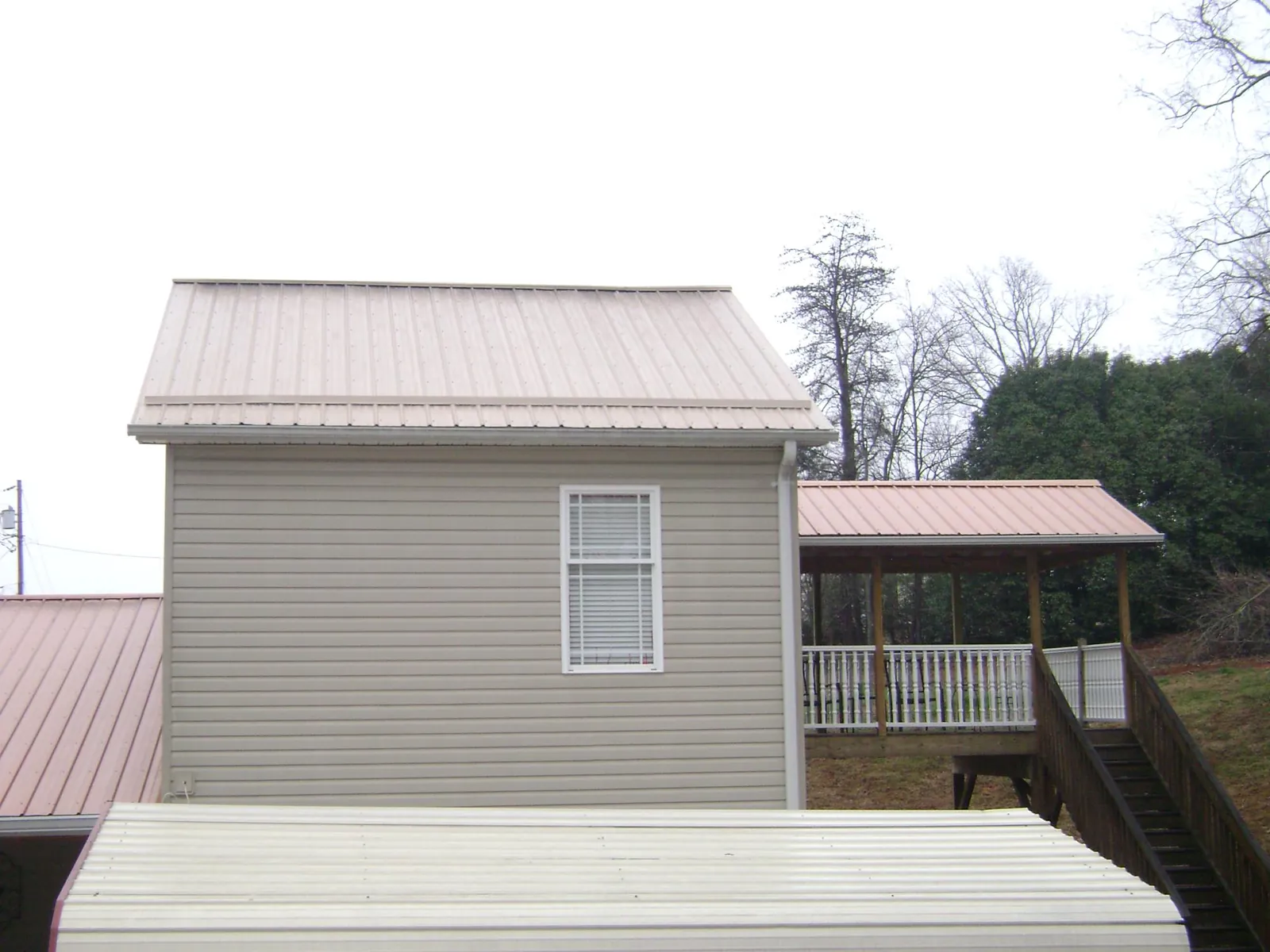 Tan metal roofs on a two story addition and attached porch, from a Roof Replacement job in Carroll